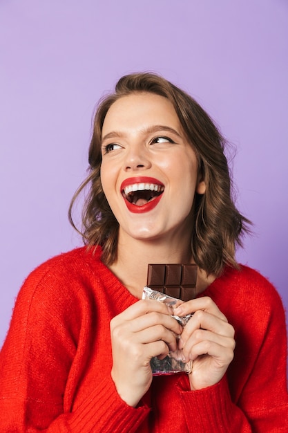 Image of a shocked emotional young woman posing isolated over purple wall wall holding chocolate.