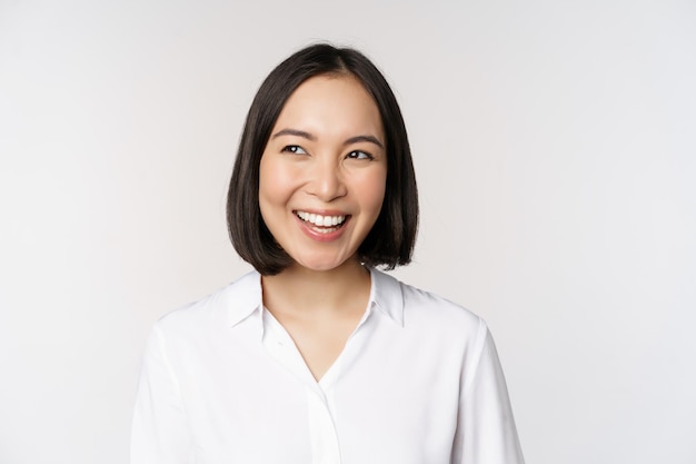 Image of smiling asian woman planning thinking of smth daydreaming standing over white background with smug face Copy space