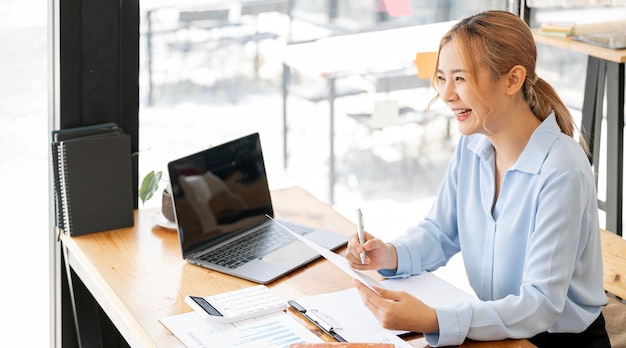 Image of smiling beautiful woman writing down notes while sitting at table in office