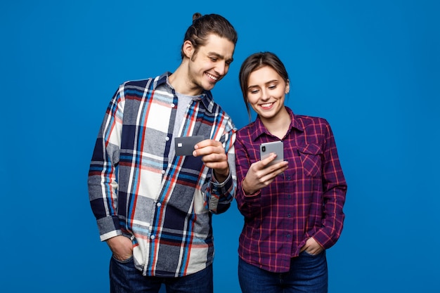 Image of smiling man and woman in casual wear standing and holding cell phones with credit card