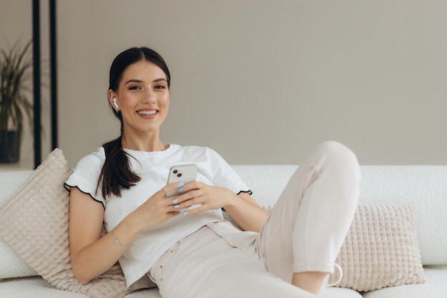 Image of a smiling woman using a mobile phone while sitting on a sofa