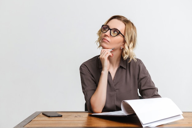 Image of thinking serious businesswoman isolated over white wall background work with clipboard with documents sit at the table.