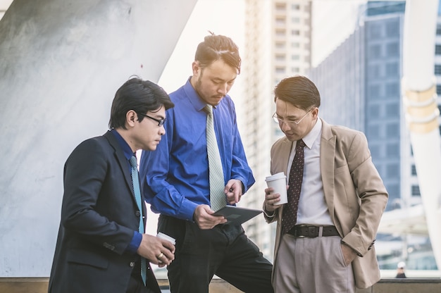 Image of three young businessmen using tablet at meeting