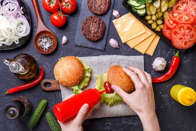 Image on top of two hamburgers and human hands adds the ketchup into the burger