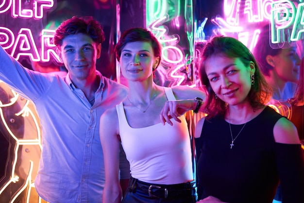 Image of two beautiful women and one man in an amusement park in a room with neon light Entertainment concept