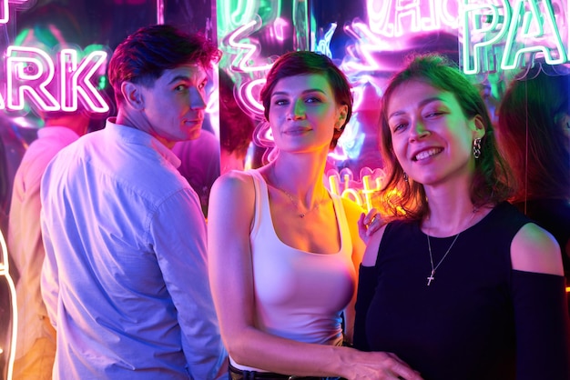 Image of two beautiful women and one man in an amusement park in a room with neon light Entertainment concept