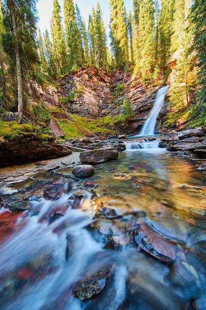 Image of View by shallow riverbed with beautiful waterfall in distance tucked into colorful mossy canyon