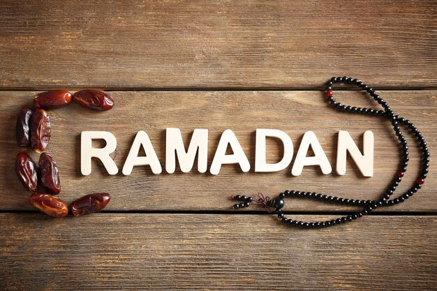 Photo image of word ramadan with rosary and dates fruit on wooden background close up