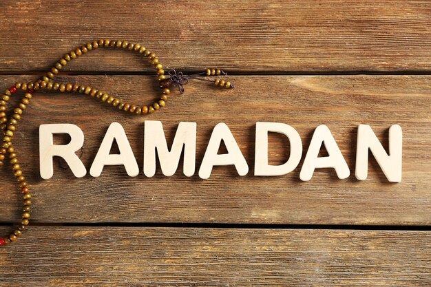 Photo image of word ramadan with rosary on wooden background close up