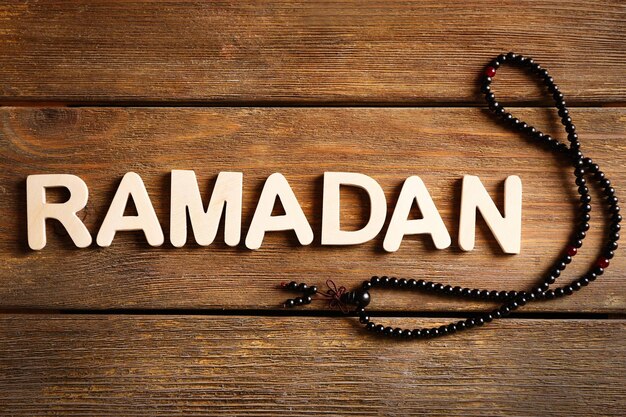 Photo image of word ramadan with rosary on wooden background close up