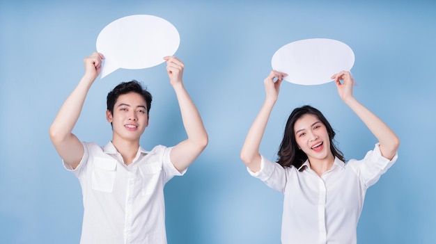 Image of young Asian couple holding message bubble on blue background