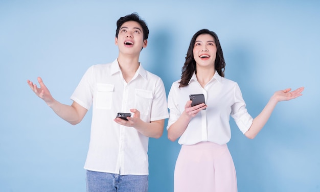 Image of young Asian couple using smartphone on blue background