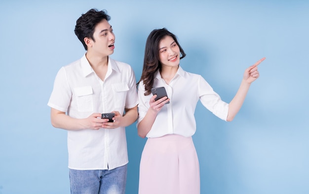 Image of young Asian couple using smartphone on blue background