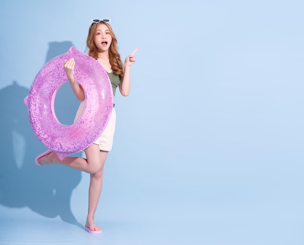 Image of young Asian girl holding swimming float on blue background summer vacation concept