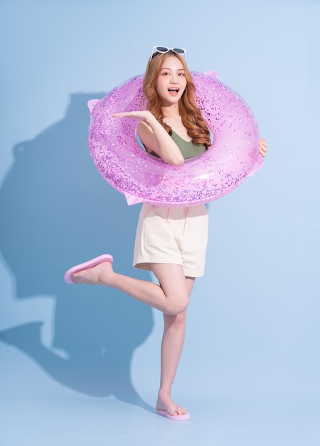 Image of young Asian girl holding swimming float on blue background summer vacation concept