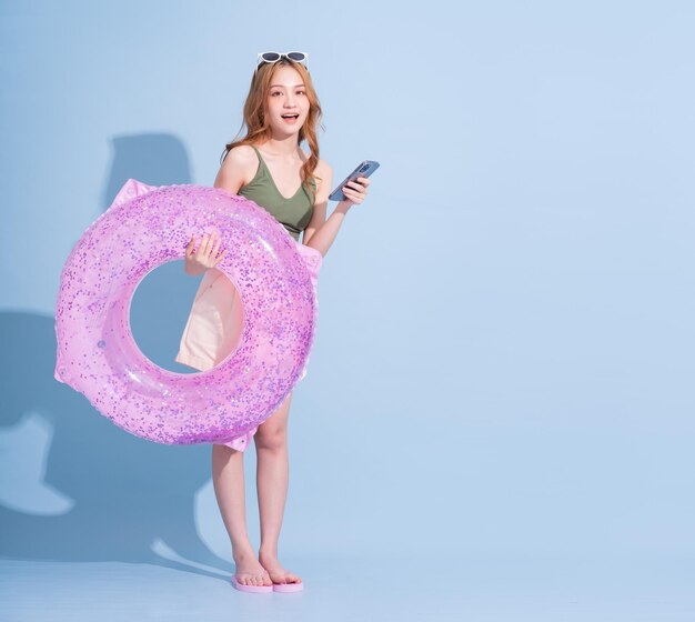 Image of young Asian girl holding swimming float on blue background summer vacation concept