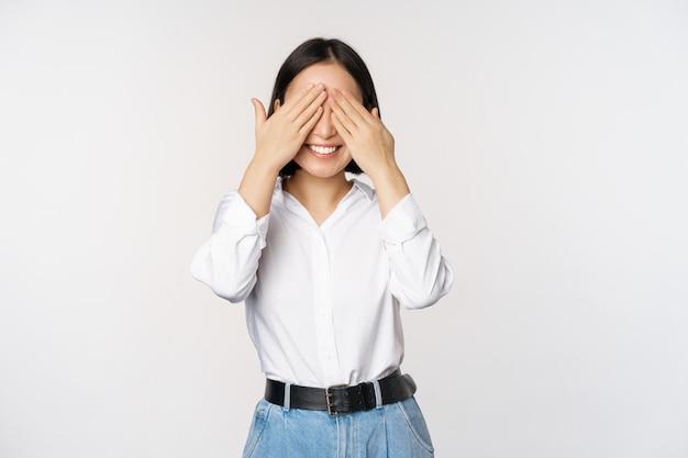 Image of young asian woman close her eyes and smiles waits for surprise anticipates stands over white background