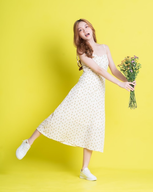 Image of young Asian woman holding flowers on yellow background