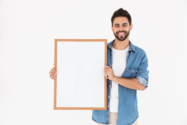 Photo image of young bearded man holding empty placard in frame and smiling isolated over white wall