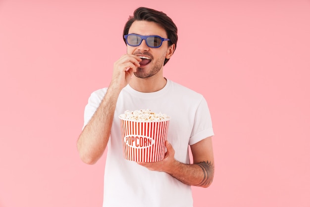 Image of young funny man wearing 3d glasses eating popcorn while watching movie isolated