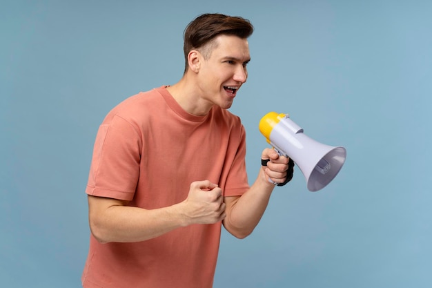 Image of young handsome man standing over blue background and screaming with mouthpiece