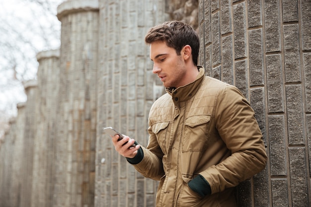 Image of young man walking on the street and chatting by his phone outdoors. Look at phone.