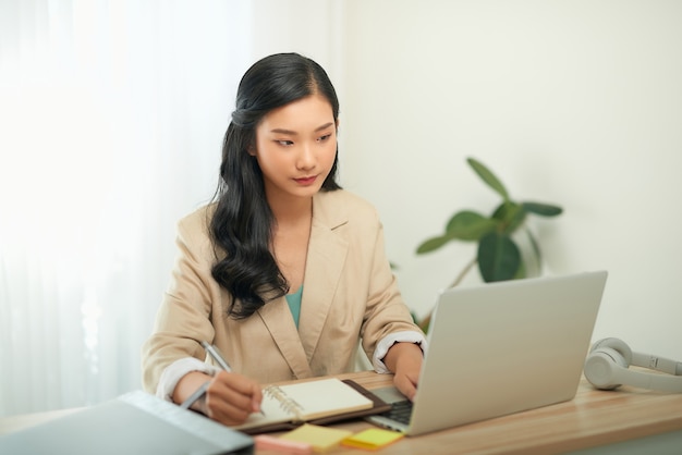 Image of young pleased happy cheerful cute beautiful business woman sit indoors in office using laptop computer