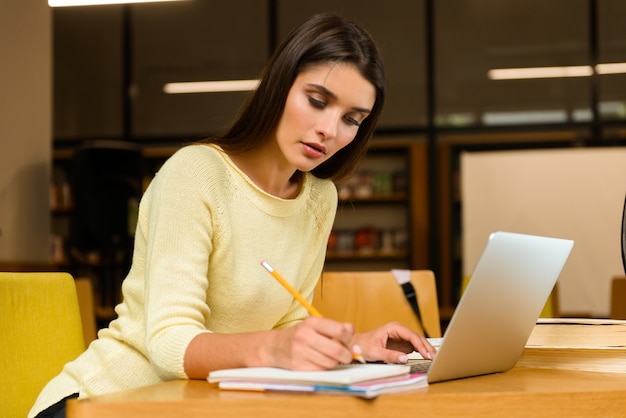 Image of a young student concentrated woman in library doing homework studying read and using laptop computer.