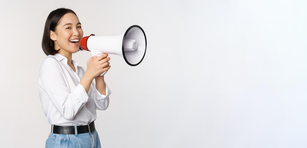 Image of young woman korean activist recruiter screaming in megaphone searching shouting at loudspeaker standing over white background