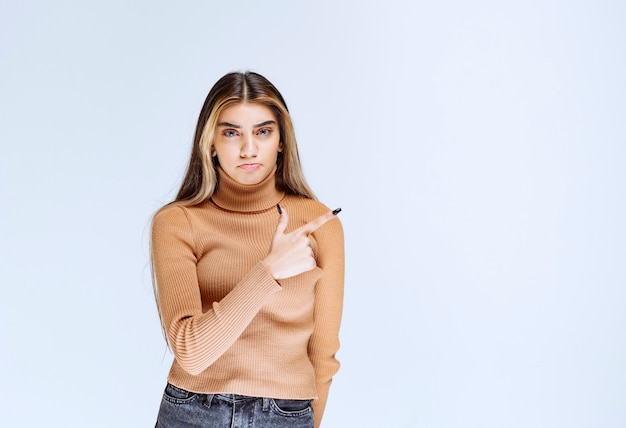 Image of a young woman model in brown sweater standing and pointing away.