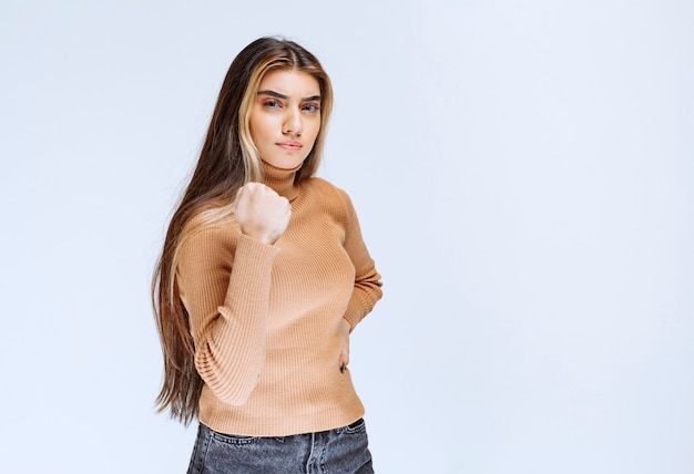 Image of a young woman model in brown sweater standing and showing fist .