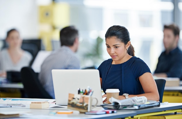 Immersed in her work Shot of a designer sitting at her desk working on a laptop with colleagues in the background