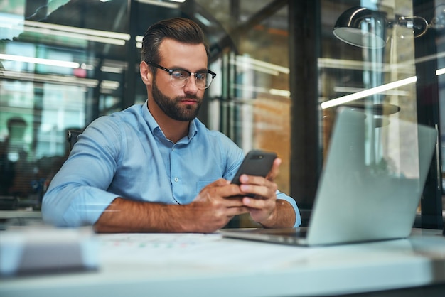 Important call portrait of young focused businessman in eyeglasses and formal wear looking at his