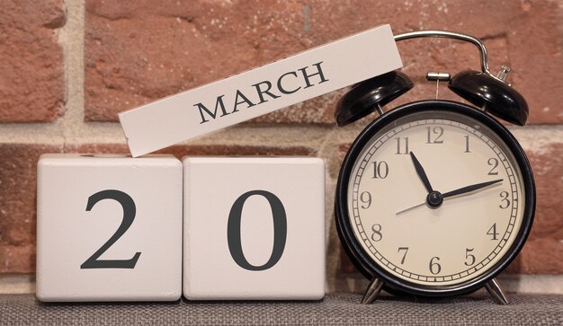 Photo important date, march 20, spring season. calendar made of wood on a background of a brick wall. retro alarm clock as a time management concept.