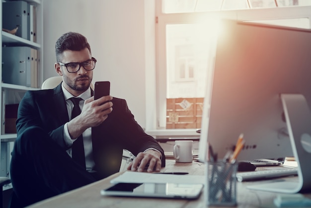 Important message. Handsome young man in formalwear using his smart phone while sitting in the office