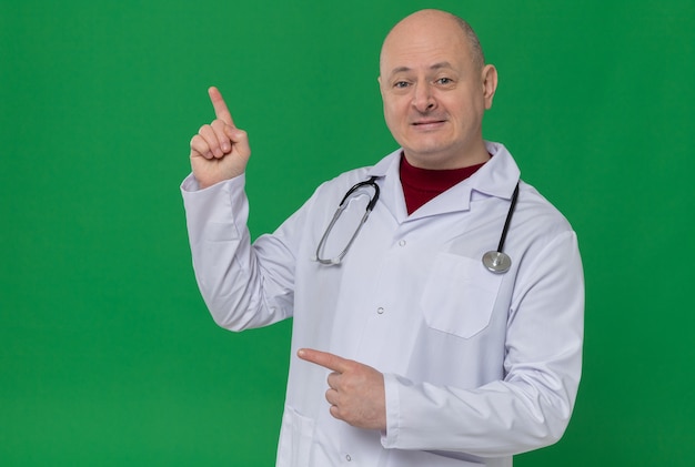 Impressed adult man in doctor uniform with stethoscope pointing up and at side 