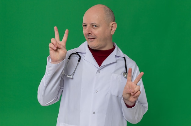 Impressed adult slavic man in doctor uniform with stethoscope gesturing victory sign