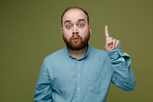 Impressed points at up young handsome guy wearing blue shirt isolated on green background