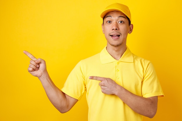 Impressed young delivery man wearing cap and uniform pointing up at corner 