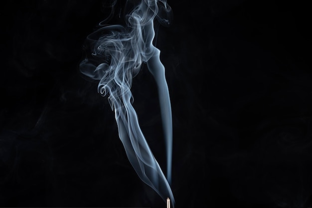 Incense stick with smoke against black background