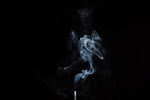 Incense stick with smoke against black background