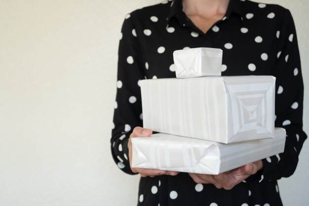 Incidental woman holding Christmas gifts, selective focus, light background and copy space.