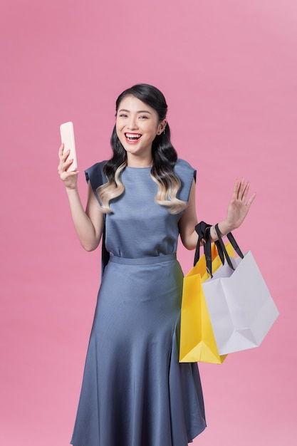 Incredibly excited young woman holding smartphone and shopping bags looking at camera in surprise