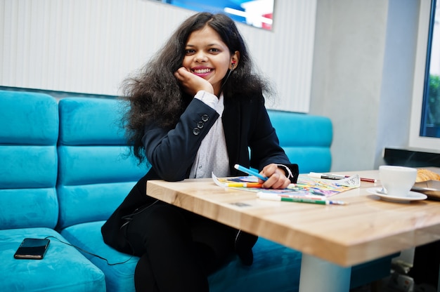 Indian artist woman wear formal paint picture and listening hindu music from earphones,while sitting at cafe.