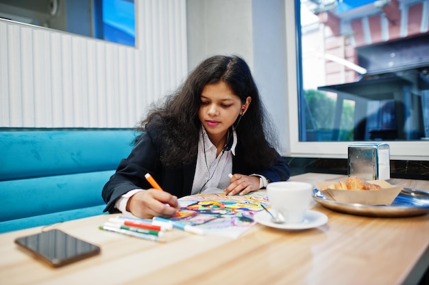 Indian artist woman wear formal paint picture and listening hindu music from earphoneswhile sitting at cafe