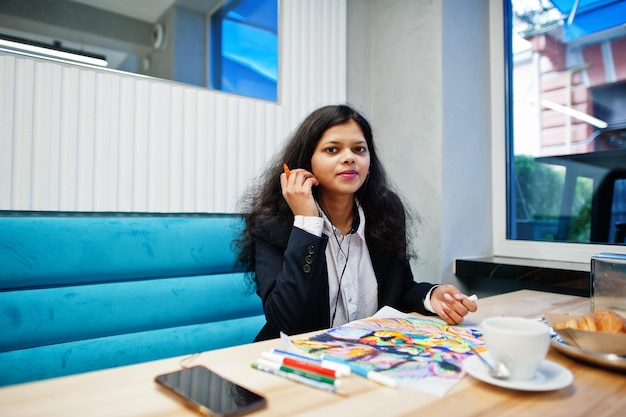 Indian artist woman wear formal paint picture and listening hindu music from earphoneswhile sitting at cafe