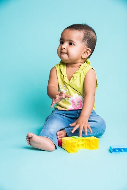 Indian or Asian Toddler or Infant or baby playing with toys or blocks while lying or sitting isolated over bright or colourful background