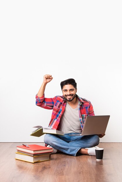 Indian asian university or college student sitting with laptop computer with books on wooden floor against white background