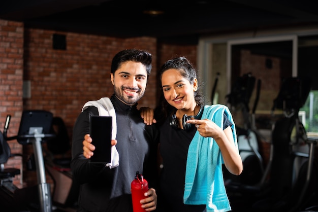 Indian asian Young couple is working out in the gym. Attractive woman and handsome fit man are training in modern gym - health and fitness concept