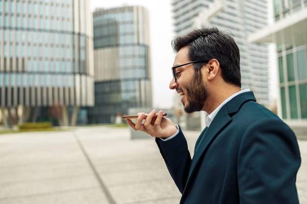 Indian businessman is recording audio message to client standing near office during break